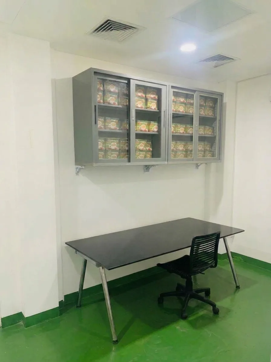 In-Process Quality Control & Product Retention Room: glass-front cabinets holding product boxes above a table and black chair.